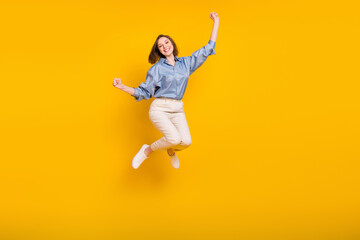 Fototapeta na wymiar Photo of funny lucky young lady dressed blue outfit jumping high rising fists smiling isolated yellow color background