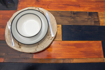 An old wooden recycled table top taken with a plate and knife and fork on a tree trunk mat