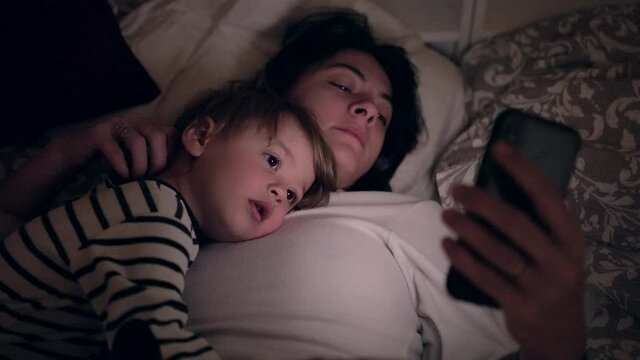Mother and baby child lying in bed watching media entertainment at night