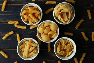 Bowls with uncooked pasta on wooden background