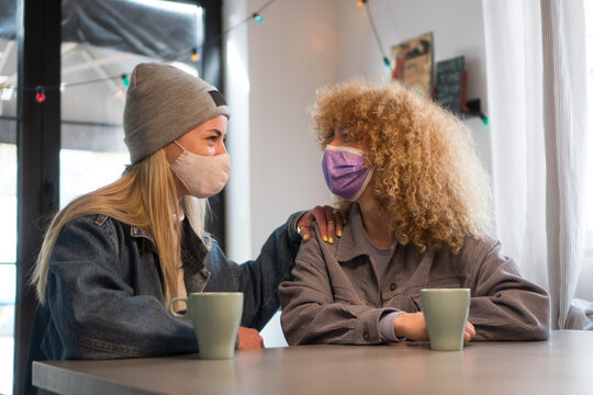 Two Teenage Girls Are Hanging Out In A Coffee Shop With Their Protective Face Masks On.