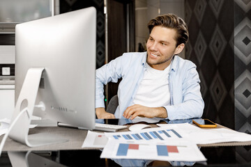 Handsome young businessman is having a video meeting with colleagues, sitting at the desk, using computer. Happy stylish male freelancer talking with coworkers, smiling, communication concept