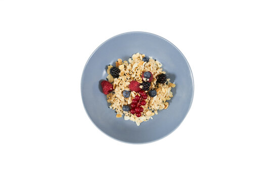 Top view of appetizing oatmeal with fresh berries and nuts in beautiful blue plate on white background. Concept of tasty porridge to support the figure or for emaciation. 