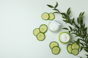 Jars with cosmetic cream, cucumber slices and branch on white table