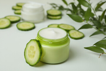 Jars with cosmetic cream, cucumber slices and branch on white table