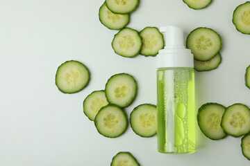 Bottle with cosmetics and cucumber slices on white background