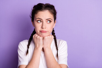 Photo of dreamy upset young woman look empty space hold fists chin think isolated on purple color background