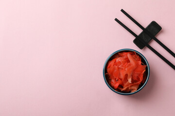 Bowl with red pickled ginger and chopsticks on pink background