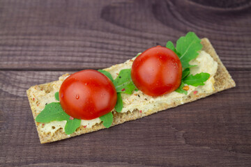 Thin crunchy crouton with arugula and ripe cherry tomatoes, hummus. Vegan vegetarian snack, snack with croutons and fresh vegetables