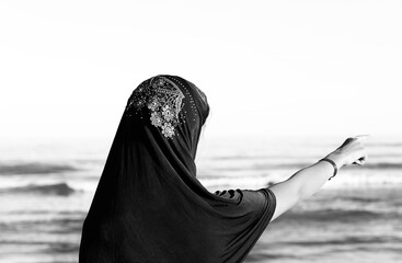 young girl with veil to cover her head by the sea points away with black and white effect