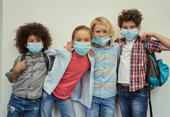 Best friends. Four adorable diverse kids wearing protective face masks looking at camera, posing together over light background