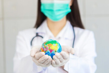 Asian woman doctor wears medical coat, face mask and rubber glove while holds global ball as sign...
