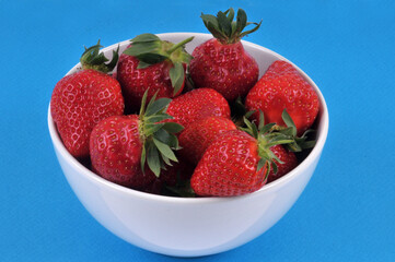 Bol de fraises gariguettes en gros plan sur fond bleu