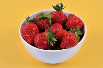 Bol de fraises gariguettes en gros plan sur fond jaune