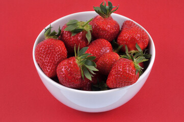 Bol de fraises gariguettes en gros plan sur fond rouge