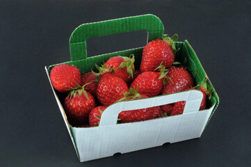 Barquette en carton de fraises gariguettes en gros plan sur fond noir