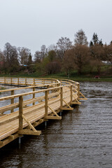 Naklejka premium A new wooden boardwalk above the pond water, dark waves, cloudy skies.