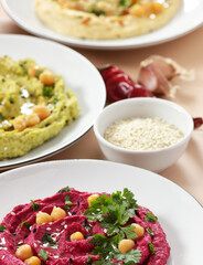 Variety of colored hummus: red, green, yellow - vegan lebanese meal, from above overhead top view, banner or background texture, vegan and vegetarian protein food, assortment of bean meal concept