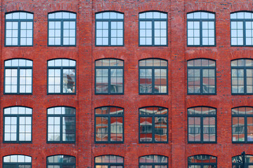 Fototapeta premium Close-up of a wall of a factory building. Red brick, mirrored windows. 