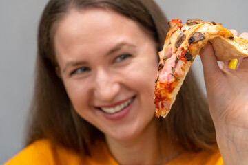 Close-up of a beautiful, happy, smiling young woman holding a slice of pizza in her hand and looking at it with adoration close-up. Focus on pizza