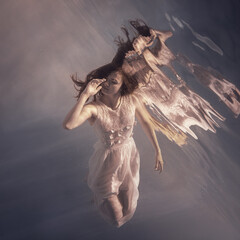 A girl in a white dress with long dark hair swims underwater as if floating in weightlessness