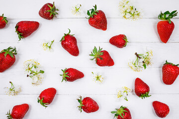 Fresh juicy strawberries and natural flowers on a white wooden background. Top view, place for text. Food background.