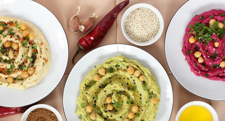 Variety of colored hummus: red, green, yellow - vegan lebanese meal, from above overhead top view, banner or background texture, vegan and vegetarian protein food, assortment of bean meal concept