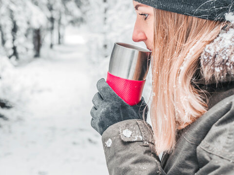 Tea keeps girl warm outside. Young woman enjoying hot drink in winter. Spruce Tree Forest Covered by Snow in Winter Landscape on the background . image for wallpaper. Copy space