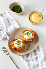 Delicious hearty breakfast, eggs Atlantic in a plate on a white background, round fried bun with salmon and eggs Benedict, hollandaise sauce and green onions