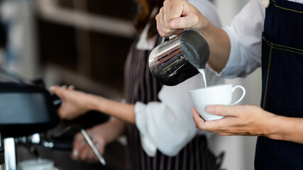 Close up hamd. Young Asian man pouring milk into coffee making espresso. Professional barista preparing coffee on counter. Barista making cappuccino, bartender preparing coffee drink.