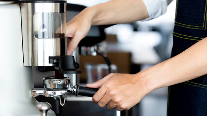 close up photo of male hands holding a metal tamper and a portafilter with coffee in a coffee shop. A man barista preparing for pressing ground coffee for brewing espresso or americano in a cafe.