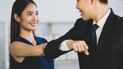 Happy ethnic coworker bumping elbows while greeting each other in office