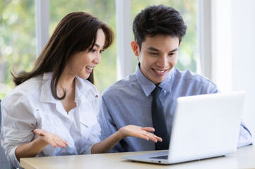Obraz premium Beautiful black long hair Asian businesswoman and gook looking cute Asian businessman sitting together and watching the screen of laptop notebook computer in office with smile face