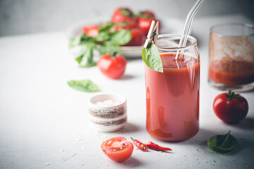 Glass of tomato juice with basil and fresh tomatoes on white background