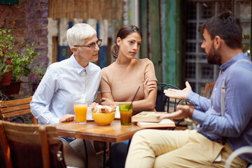 The young man defends himself from a verbal attack by his female friends of different generations while they having a drink at a bar. Leisure, bar, friendship, outdoor