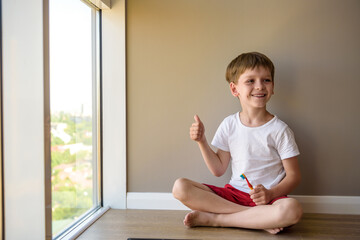 Baby sitting on a wooden floor of his house nibbling a toothbrush, while learning to brush his teeth.