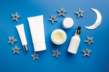 Cosmetic white containers on blue background top view. Skin care cosmetology products, night care...