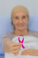 A middle-aged breast cancer patient lay on the bed and showing the pink ribbon symbol of breast cancer