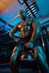 Fototapeta na wymiar Bodybuilder athlete trains in the gym. Sporty muscular guy with athletic kettlebell. Sport and fitness motivation. Individual sports recreation with bodybuilding.