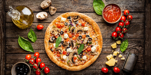 Tasty vegetable pizza and cooking ingredients tomatoes and basil on wooden background. Top view