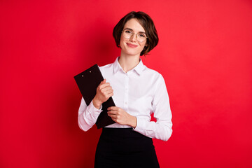 Naklejka premium Photo of happy positive lovely charming secretary in glasses hold organizer smiling isolated on red color background