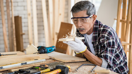 Elderly craftsman blowing wooden dust from board