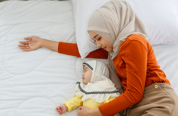 A cute and beautiful Asian Muslim in hijab holding and hugging her baby daughter and sleep with her