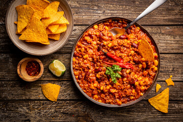 Mexican hot chili con carne in a bowl with tortilla chips on dark background, top view