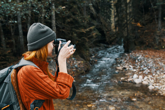 woman with a camera on nature in the mountains near the river and tall trees forest landscape