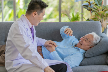 Obraz premium An old fat asian male patient with white gray hair wearing light blue shirt laying down on gray sofa laughing and use his left index finger pointng young doctor wearing white lab coat sitting on sofa