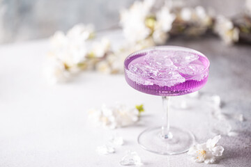 Fototapeta na wymiar Purple drink with ice cubes in a glass on white background with flowers