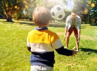 Naklejka premium family, fatherhood and people concept - happy father and little son with ball playing soccer at summer park