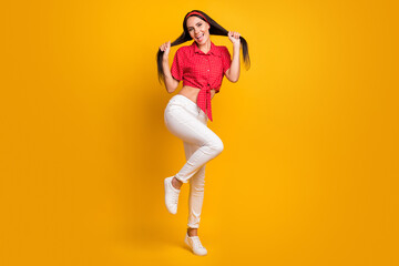 Full length photo of tricky adorable young girl dressed red shirt dancing holding hair isolated yellow color background