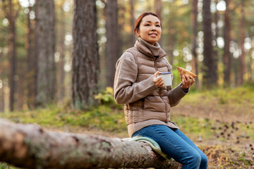 picking season, leisure and people concept - young asian woman drinking tea and eating sandwich in autumn forest